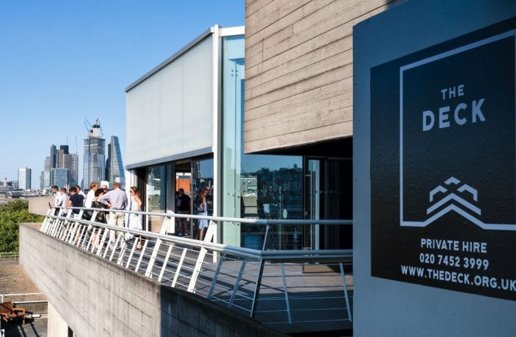 The Buffini Chao Deck event hire space: the terrace with people and a poster announcing The Deck