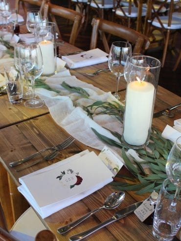 Wedding table setting with cutlery, glassware and candles and a white table runner decorated with green leaves