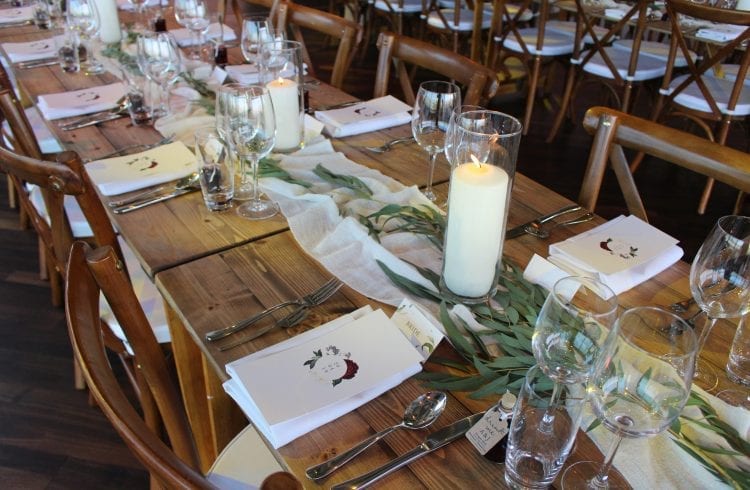 Wedding table setting with cutlery, glassware and candles and a white table runner decorated with green leaves