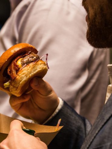 Close-up photo of a man holding a small burger and cardboard tray.