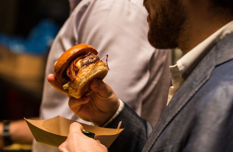 Close-up photo of a man holding a small burger and cardboard tray.