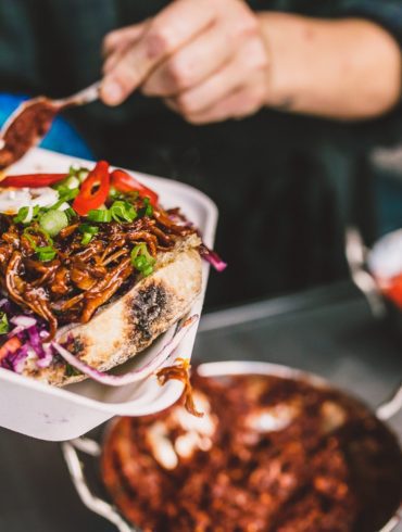 Adding sauce to a vegetable-filled wrap in a take-away tray