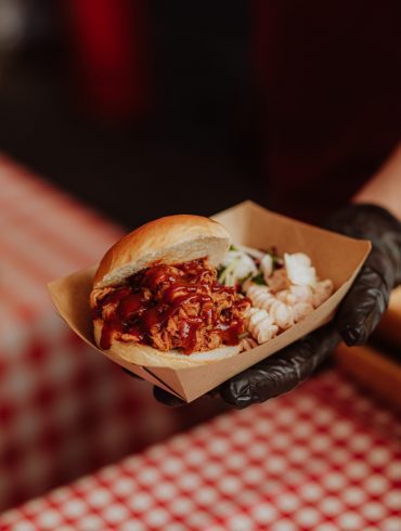 A small burger with mac 'n' cheese in a cardboard tray