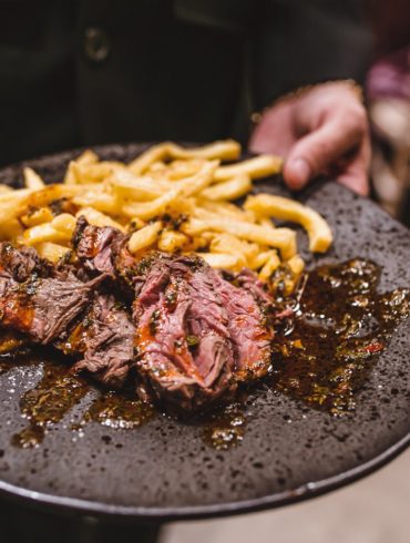 A waiter holding a plate with pulled meat and fries