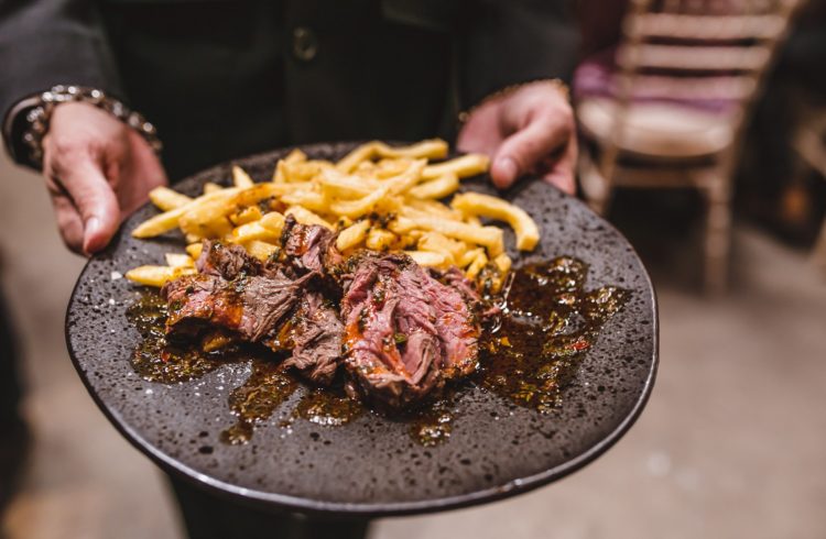 A waiter holding a plate with pulled meat and fries