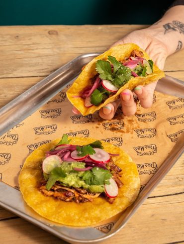 Two salad wraps, one being held, the other lying flat on a paper placemat in a steel tray