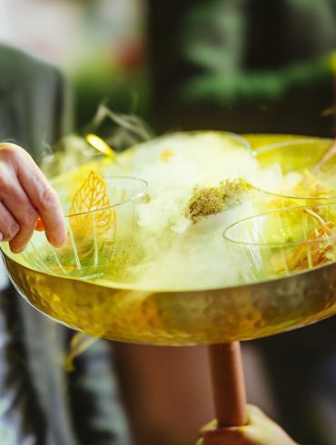 Someone takes a small bowl of food from a large serving bowl that has dry-ice smoke in its centre.