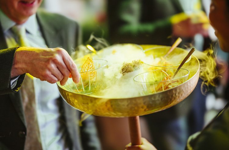 Someone takes a small bowl of food from a large serving bowl that has dry-ice smoke in its centre.