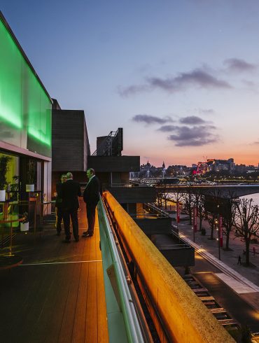 Exterior view of people standing on the terrace of the Buffini Chao Deck, overlooking the Thames and Waterloo Bridge