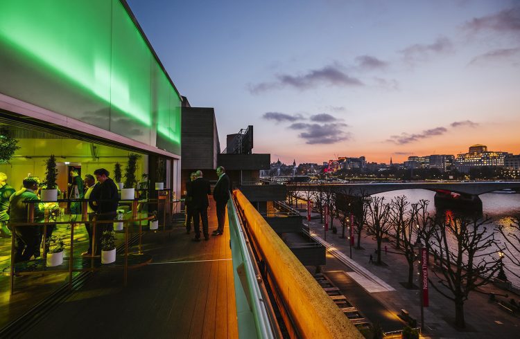 Exterior view of people standing on the terrace of the Buffini Chao Deck, overlooking the Thames and Waterloo Bridge