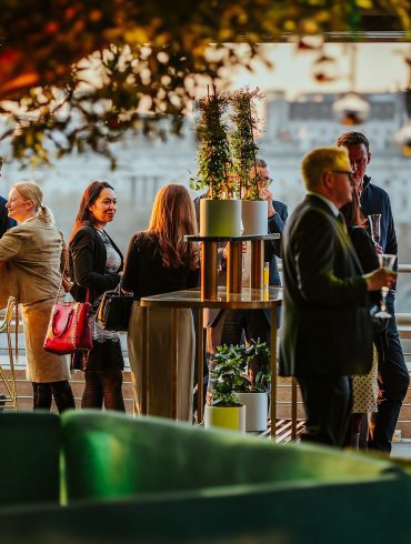 Guests stading on a terrace, with a tree i nthe interior foreground and Somerset House, out of focus, in the background.