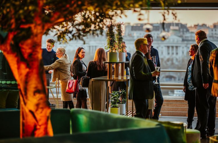 Guests stading on a terrace, with a tree i nthe interior foreground and Somerset House, out of focus, in the background.