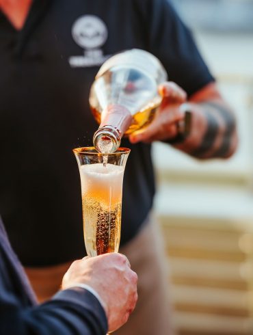 A waiter pours sparkling wine into a flute glass being held by a guest.