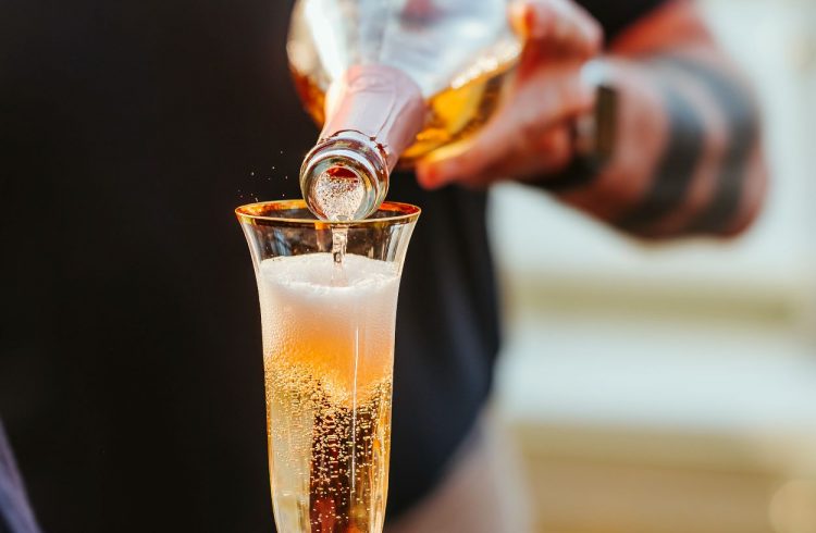 A waiter pours sparkling wine into a flute glass being held by a guest.